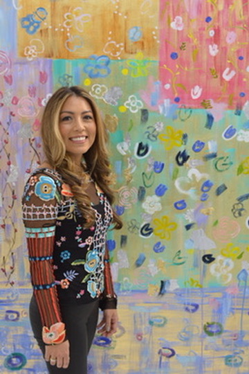 Michelle Sakhai standing in profile beside one of her large abstract paintings, wearing a floral embroidered top
