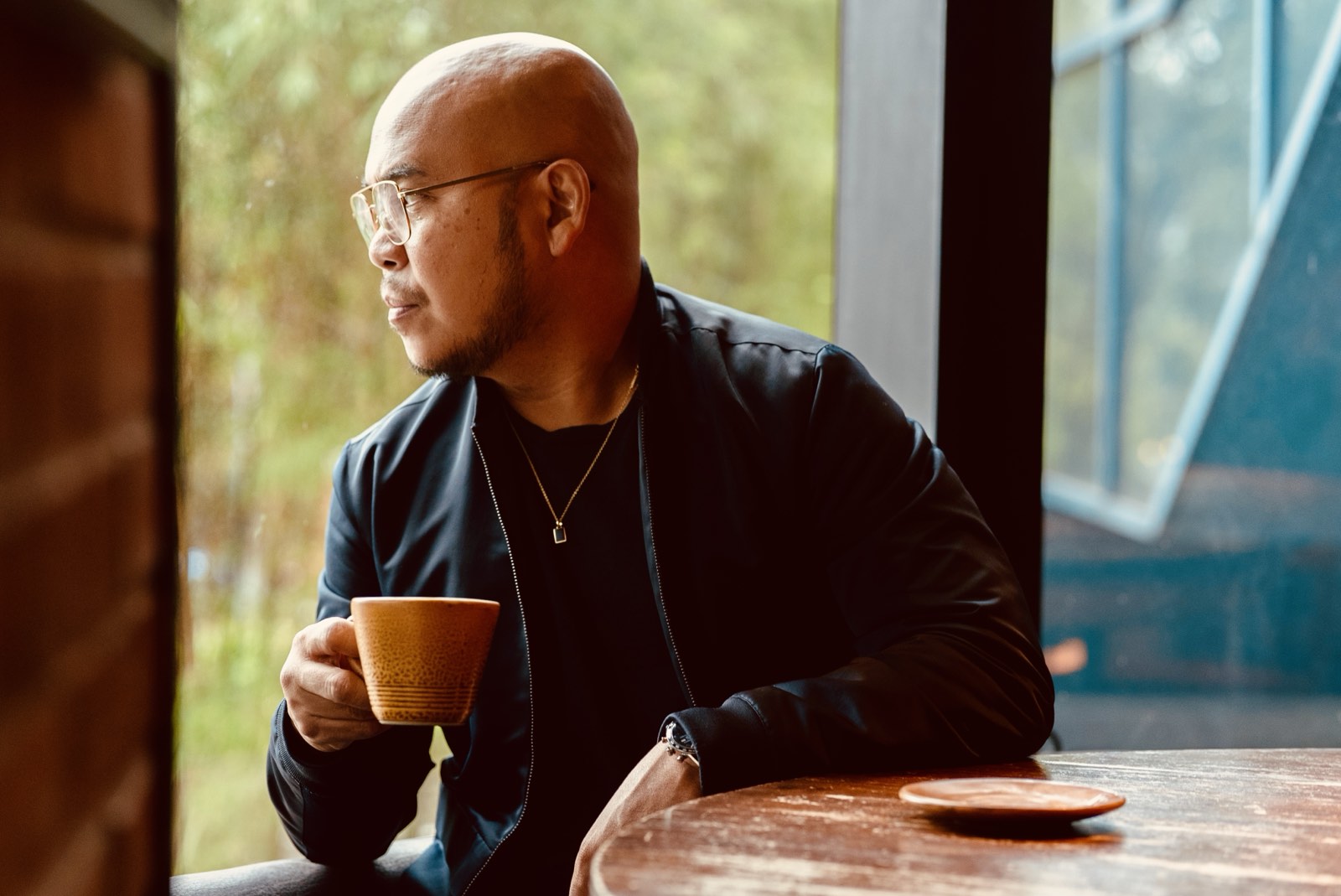 Julian P. Tarrobago Jr. holding a cup of coffee and looking out a window